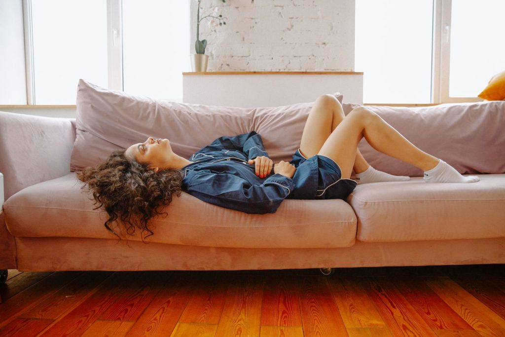 Mujer tumbada en el sofá con las manos sobre el vientre por molestias menstruales